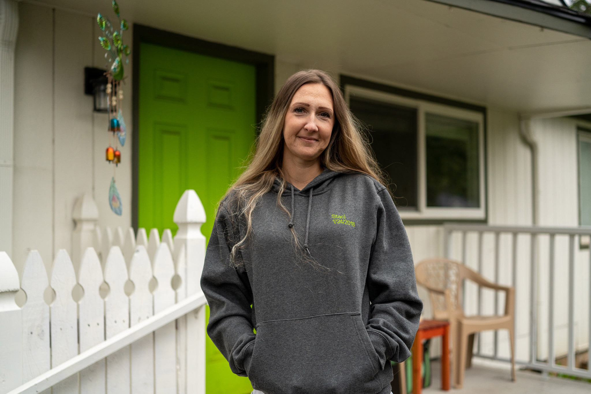a woman smiles at the camera as she stands on a porch in front of a white house with a lime green door